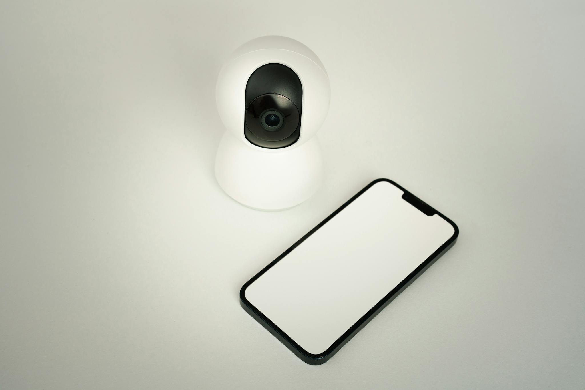 A smart home security camera paired with a blank smartphone on a white background.