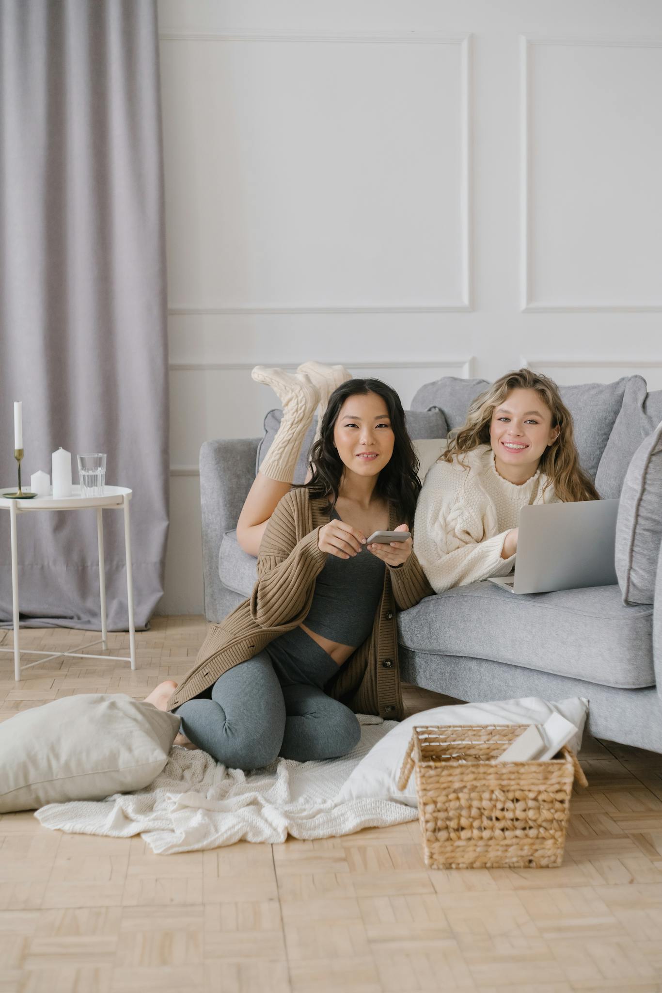 Two friends relaxing at home using a laptop and smartphone, showcasing comfort and connectivity indoors.